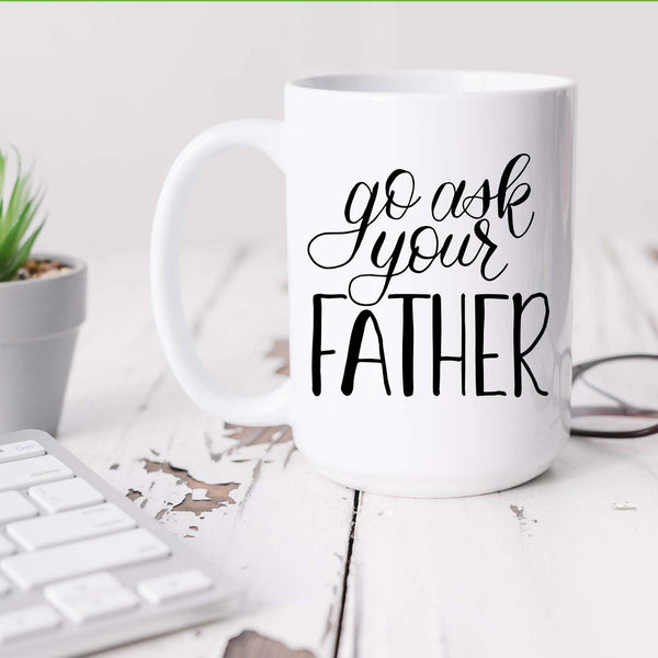 15oz white ceramic mug with hand lettered illustrated design that says go ask your father shown sitting on a white office desk