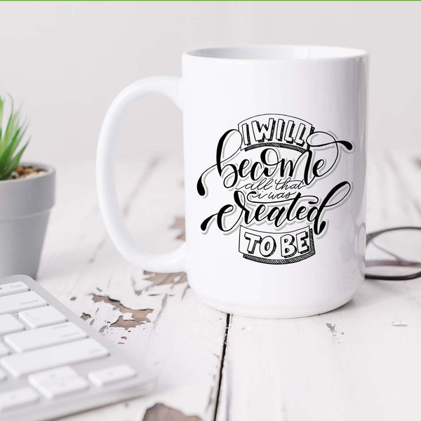 15oz white ceramic mug with hand lettered illustrated design that says I will become all that I was created to be shown on a white desk with a plant, keyboard and glasses