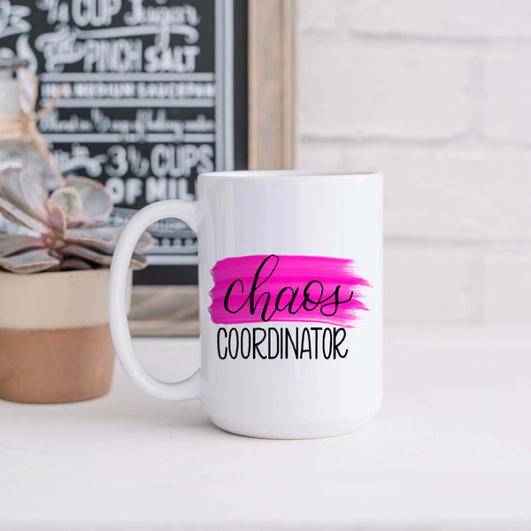 15oz white ceramic mug with hand lettered illustrated design that says chaos coordinator with a pink paint swash shown sitting in a kitchen