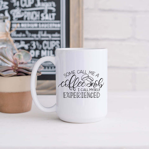15oz white ceramic mug with hand lettered illustrated design that says some call me a coffee snob I call myself experienced shown in a kitchen