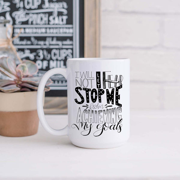 15oz white ceramic mug with hand lettered illustrated design that says I will not let fear stop me from achieving my goals shown in a kitchen with plant and sign