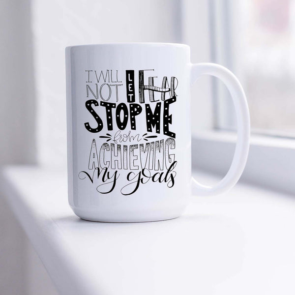 15oz white ceramic mug with hand lettered illustrated design that says I will not let fear stop me from achieving my goals shown sitting in a sunny window
