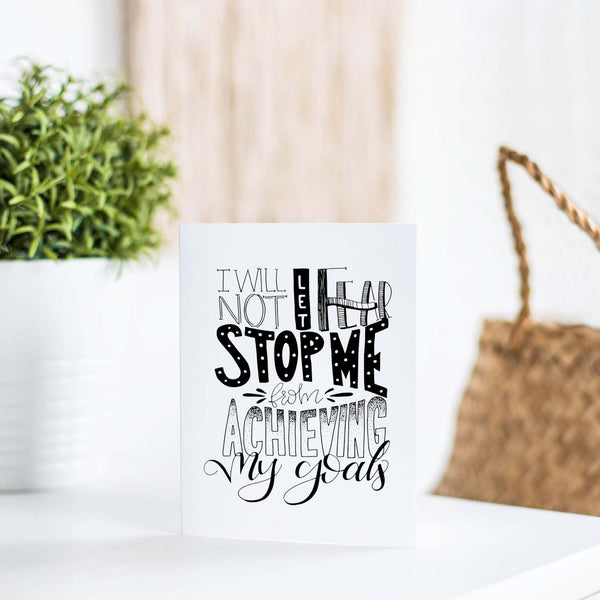 I will not let fear stop me from achieving my goals hand lettered black and white greeting card on a white folded card with A2 envelope shown on a white table with a plant and handbag