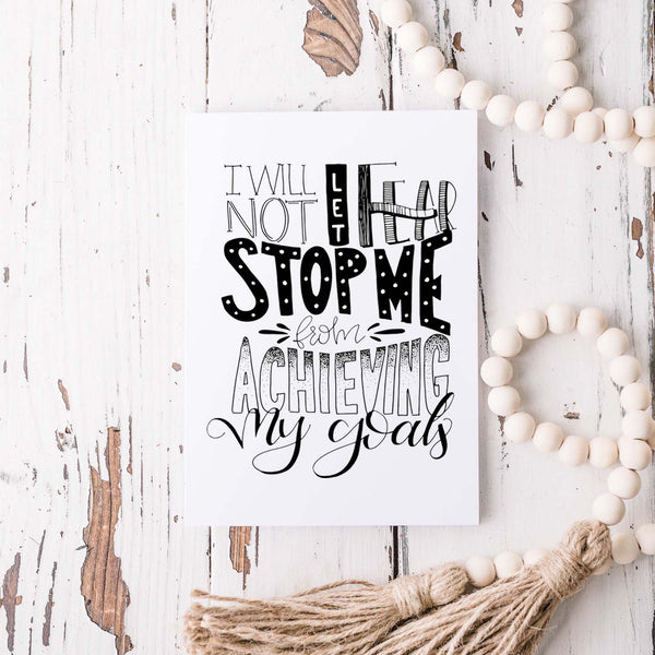 I will not let fear stop me from achieving my goals hand lettered black and white greeting card on a white folded card with A2 envelope shown on a white rustic table with a white wooden bead garland