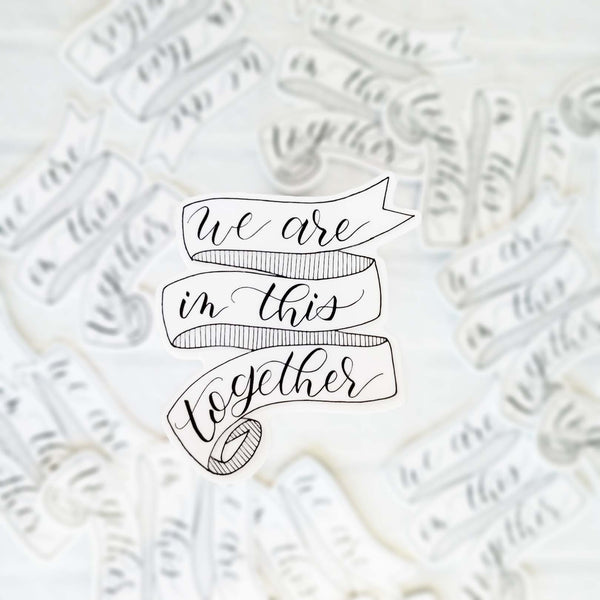 3" hand lettered, illustrated, black and white vinyl sticker that says we are in this together with a ribbon banner illustration