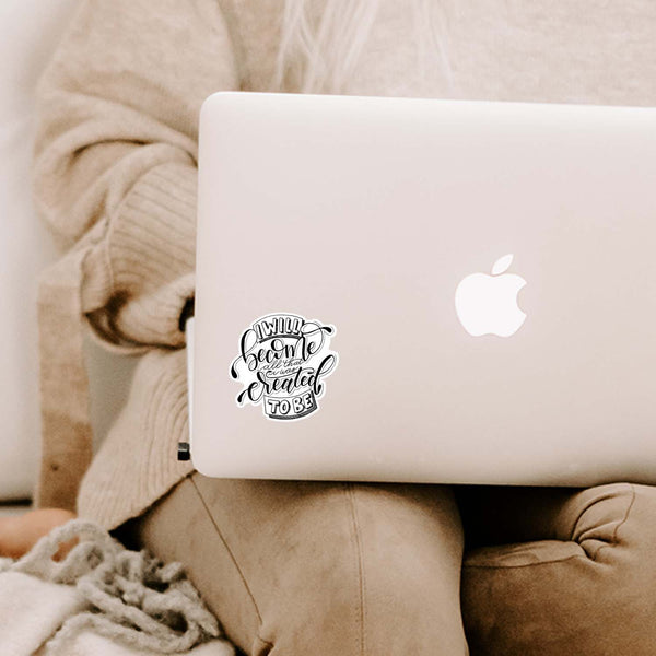 3" vinyl hand lettered illustrated sticker saying I will become all that I was created to be in black and white shown adhered to a MacBook laptop cover sitting open on a woman's lap