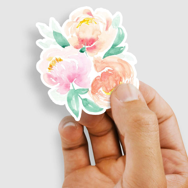 3" vinyl sticker of 3 pink and peach watercolor peonies and leaves shown with a woman's hand holding the sticker