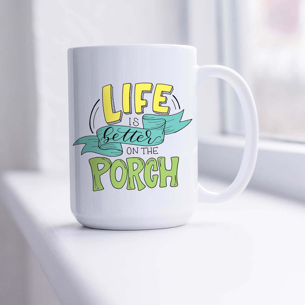 15oz white ceramic mug with hand lettered illustrated design that says Life Is Better On The Porch shown sitting in a sunny window