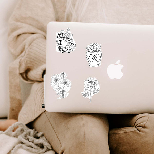 Collection of inspirational and motivational black and white stickers shown on a MacBook cover sitting open on a woman's lap