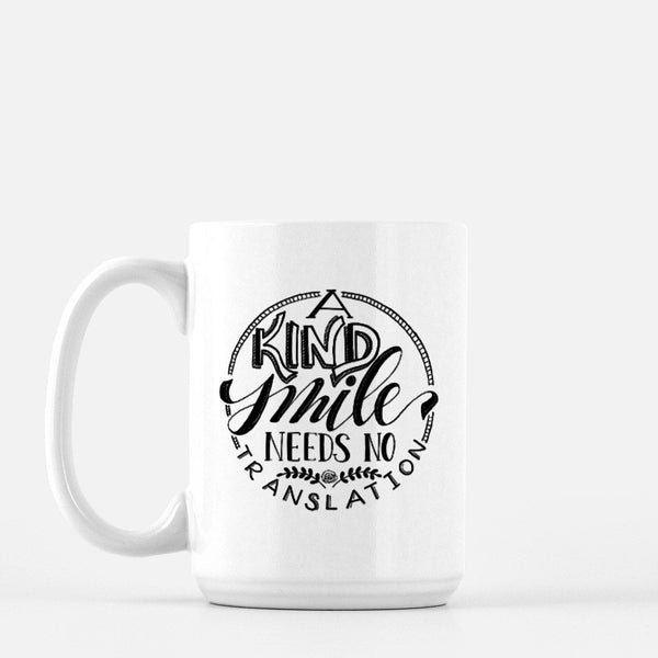 15oz white ceramic mug with hand lettered illustrated design that says a kind smile needs no translation
