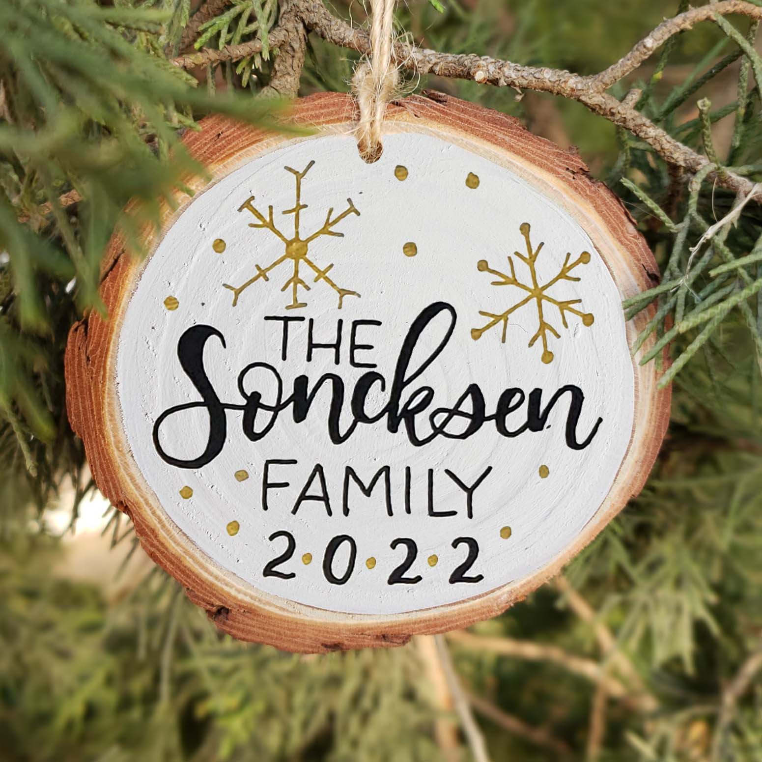 Hand painted rustic wood slice ornament with hand lettered family name and year and snowflake doodles