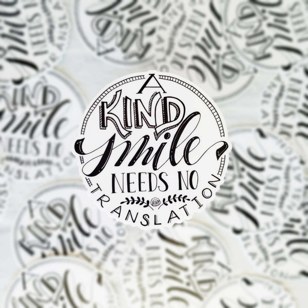 3" hand lettered illustrated vinyl sticker saying a kind smile needs no translation in black and white