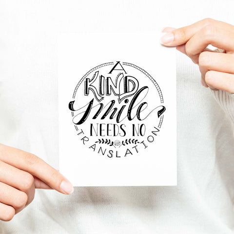 A Kind Smile Needs No Translation A2 Greeting Card black design on white card with white envelope shown with a woman in a white sweater holding card