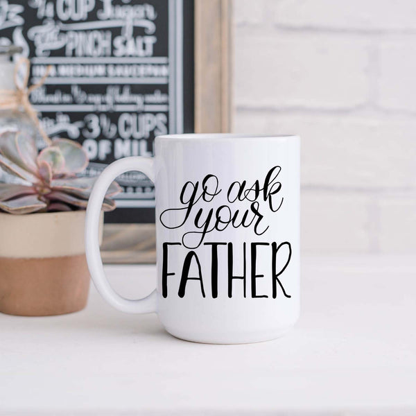 15oz white ceramic mug with hand lettered illustrated design that says go ask your father shown in a kitchen
