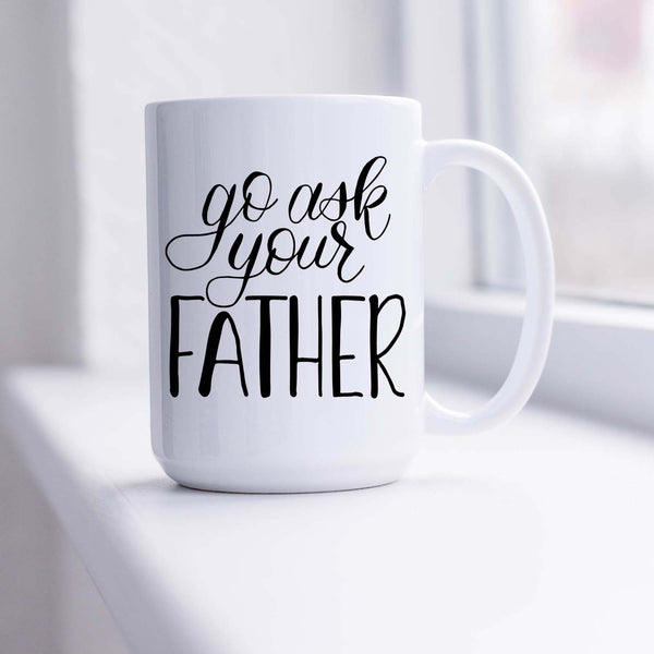 15oz white ceramic mug with hand lettered illustrated design that says go ask your father shown sitting in a sunny window