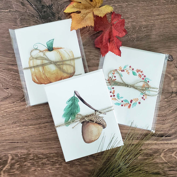 Set of 6 Watercolor painted notecards in fall autumn nature designs packaged in a clear sleeve with a jute bow shown on a wooden table