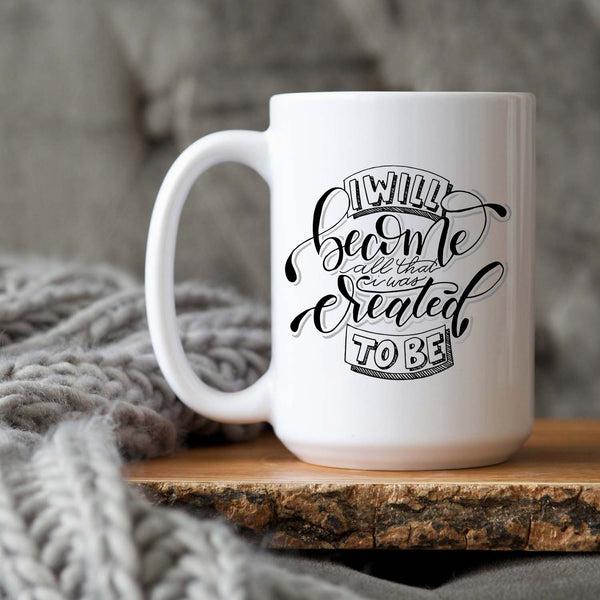 15oz white ceramic mug with hand lettered illustrated design that says I will become all that I was created to be shown on a wood tray with a grey knit blanket