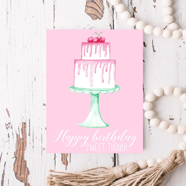 Happy birthday sweet thing watercolor birthday cake with pink frosting cherries and seafoam green cake stand birthday card shown on a rustic white wood table and white wood bead garland
