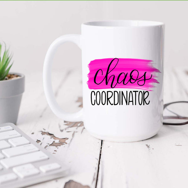 15oz white ceramic mug with hand lettered illustrated design that says chaos coordinator with a pink paint swash shown sitting on a white office desk