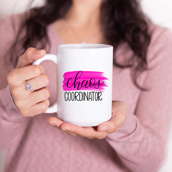 15oz white ceramic mug with hand lettered illustrated design that says chaos coordinator with a pink paint swash shown with a women holding the mug