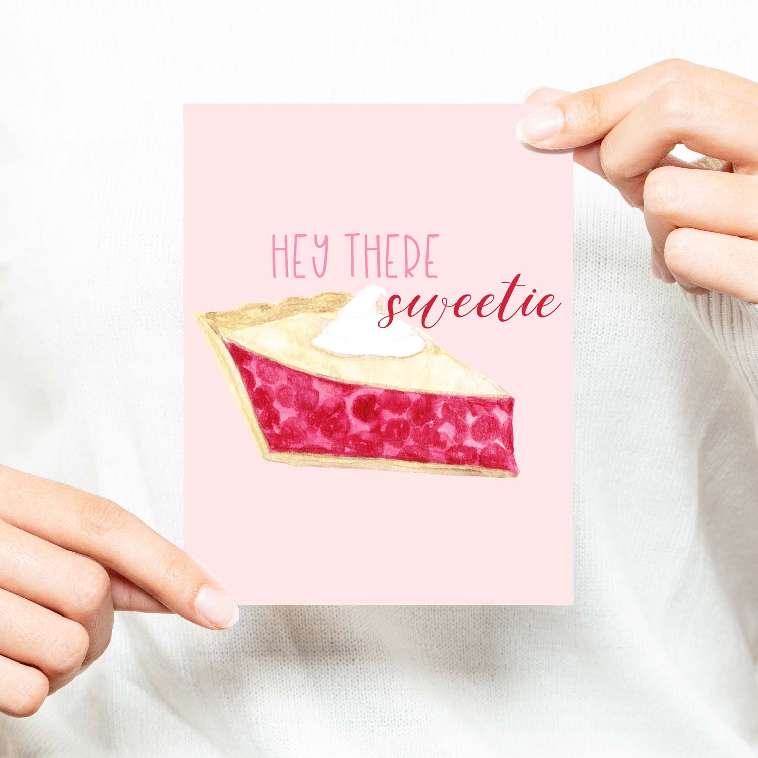 hey there sweetie watercolor greeting card with a watercolor slice of cherry pie topped with a dollop of whipped cream greeting card with white A2 envelope shown with a woman in a white sweater holding card