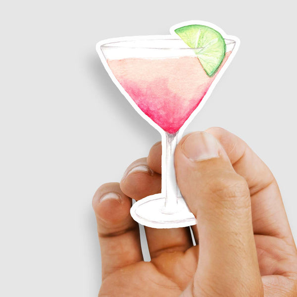 3" vinyl sticker of a watercolor martini glass with a pink cocktail and a slice of lime for garnish shown with a woman holding the sticker