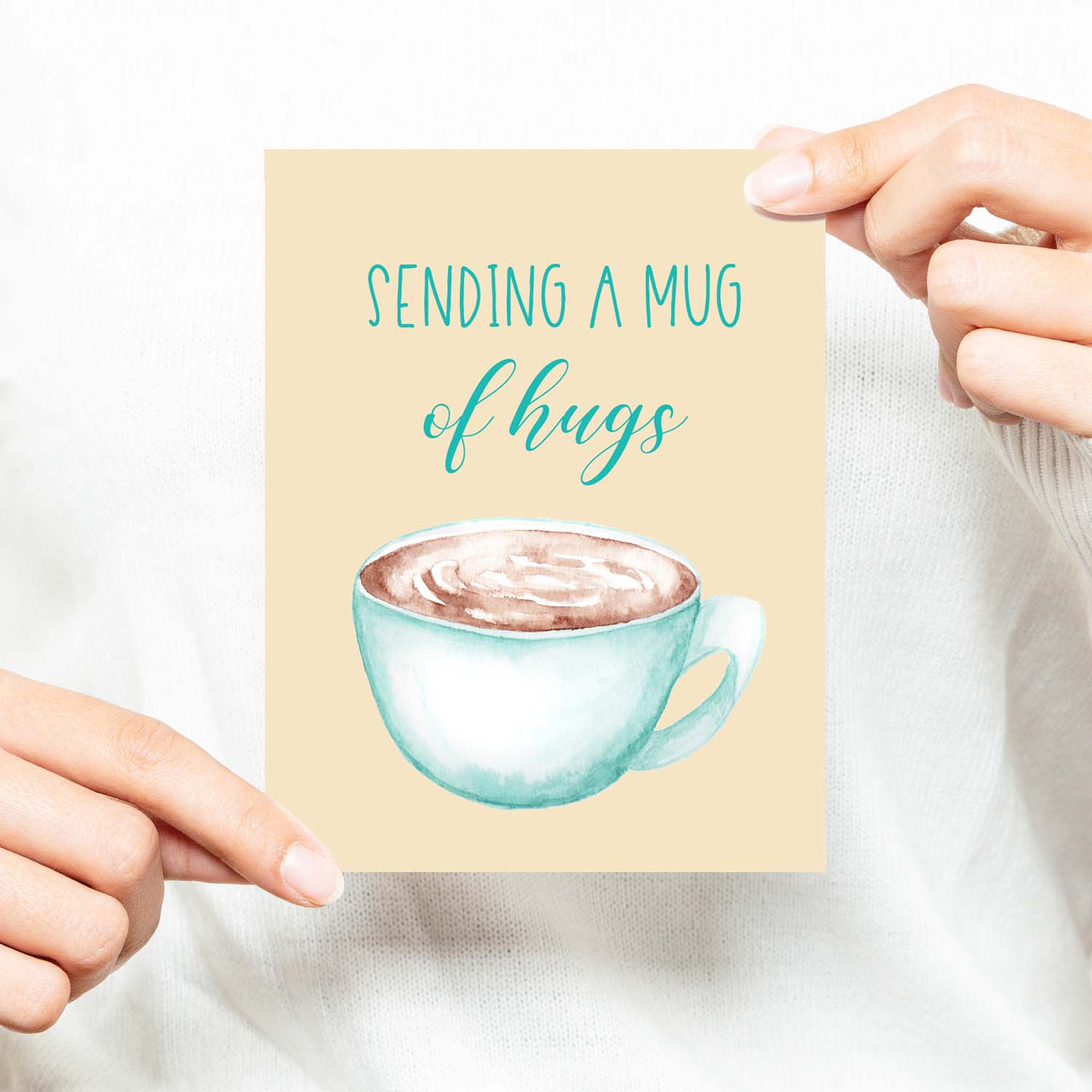 blue watercolor coffee mug filled with coffee friendship card that says sending a mug of hugs  with a white A2 envelope shown with a woman in a white sweater holding card