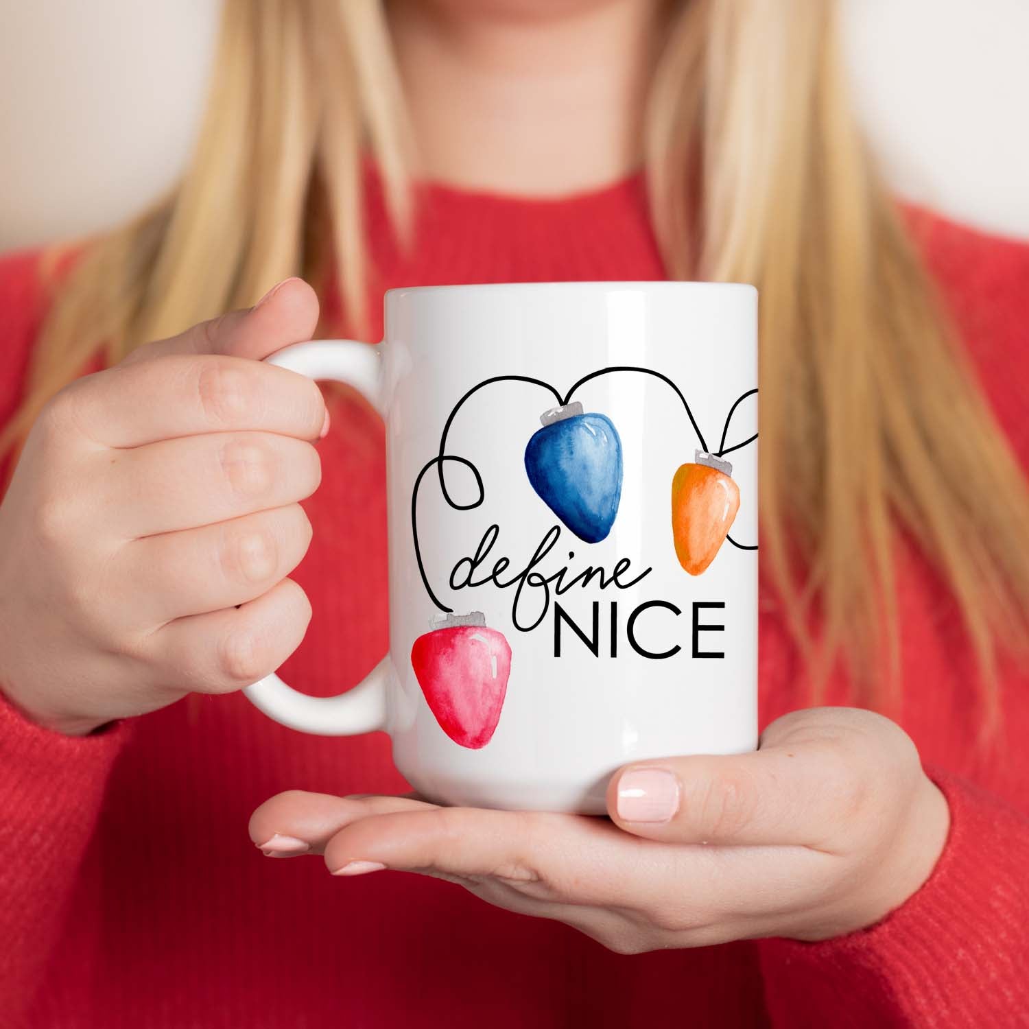 15oz white ceramic mug with watercolor string of colorful christmas lights wrapping around the cup and says define nice shown with a woman in a red holiday sweater holding the mug