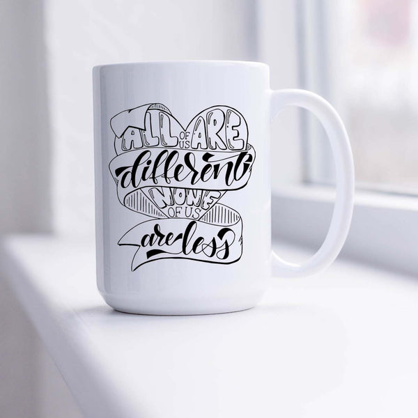 15oz white ceramic mug with hand lettered illustrated design that says all of us are different none of us are less shown in a sunny window