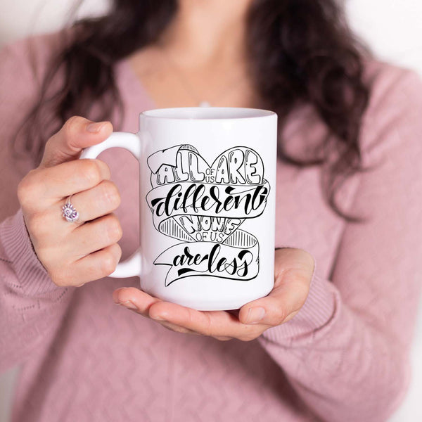 15oz white ceramic mug with hand lettered illustrated design that says all of us are different none of us are less shown with a woman holding