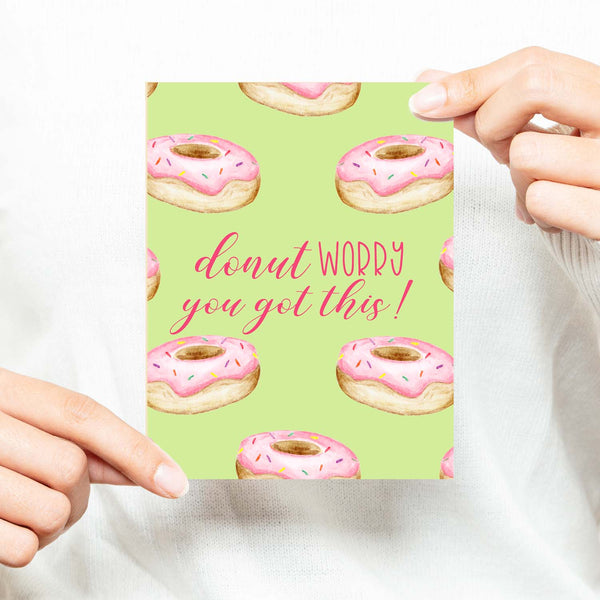 watercolor pink frosted donuts with sprinkles on a greeting card that says donut worry you got this with a white A2 envelope shown with a woman in a white sweater holding card