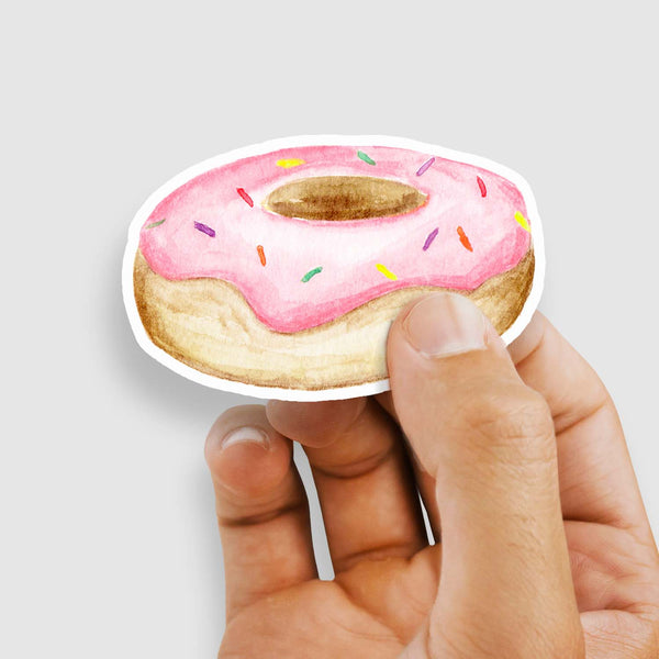 3" vinyl watercolor sticker of a a round donut with pink frosting and rainbow sprinkles shown held by a woman's hand