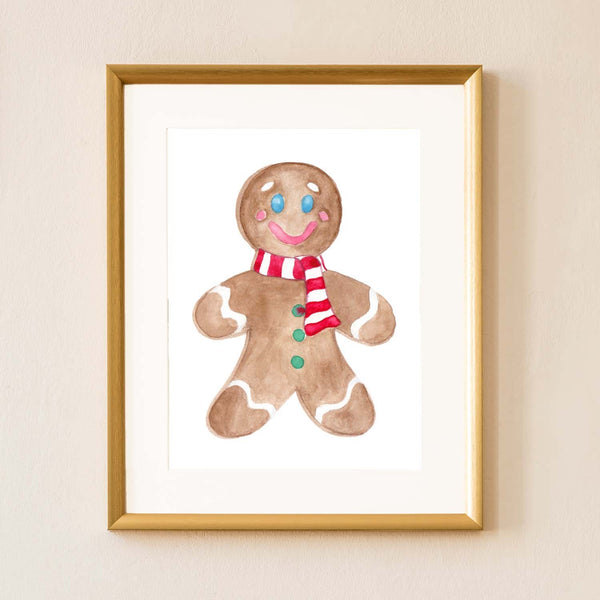 Watercolor gingerbread man painting with a red and white striped scarf shown hanging on the wall in a gold frame