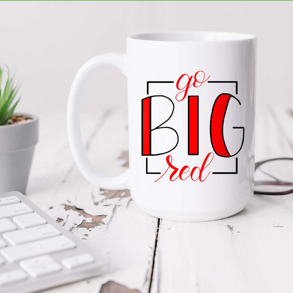 15oz white ceramic mug with hand lettered illustrated design that says Go Big Red shown sitting on a white office desk