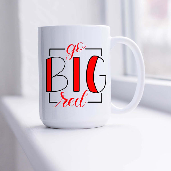 15oz white ceramic mug with hand lettered illustrated design that says Go Big Red shown sitting in a sunny window