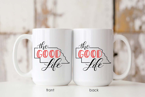 15oz white ceramic mug with hand lettered illustrated design that says The Good Life with the outline of the state of Nebraska showing both the front and back of the mug