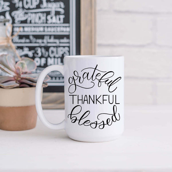15oz white ceramic mug with hand lettered illustrated design that says Grateful Thankful Blessed shown sitting in a kitchen