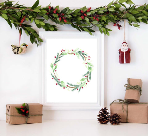 Watercolor painted holiday wreath with greens, branches and red berries shown in a white frame surrounded by christmas decorations packages