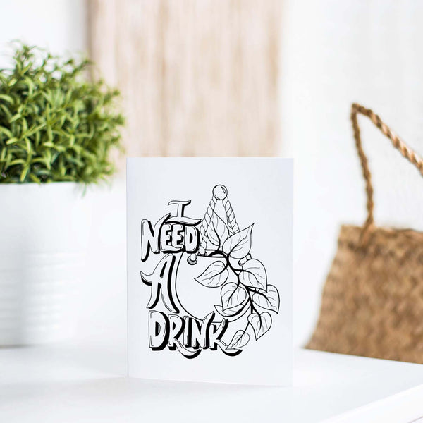 I need a drink potted pothos plant black and white illustrated greeting card on a white folded card with A2 envelope shown on a white table with a plant and handbag