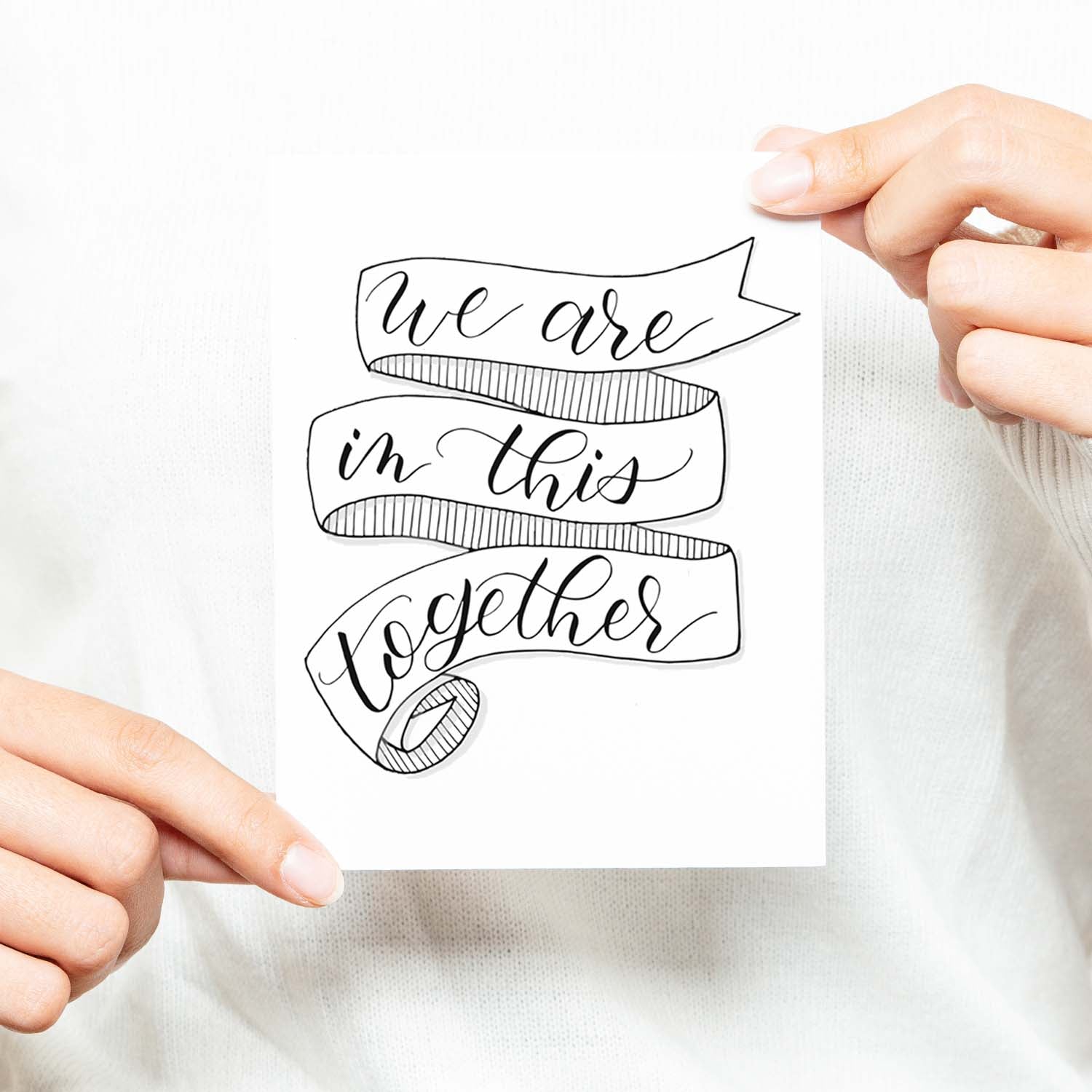 we are in this together hand lettered and illustrated black and white greeting card on a white folded card with A2 envelope shown with a woman in a white sweater holding card