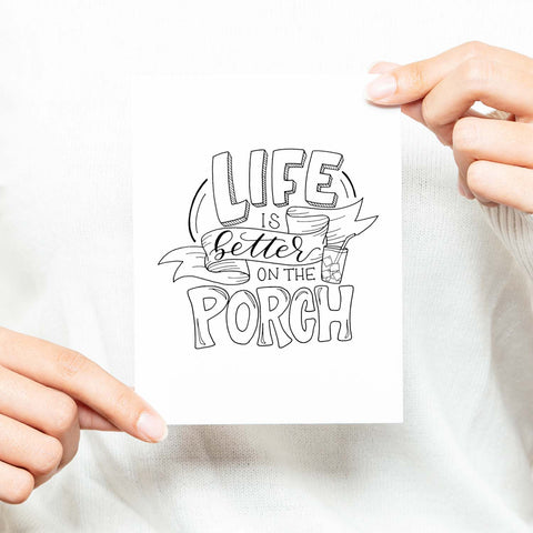 life is better on the porch hand lettered and illustrated black and white greeting card with A2 envelope shown with a woman in a white sweater holding card