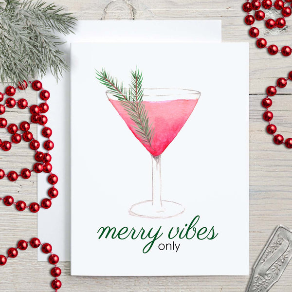 Watercolor greeting card with a watercolor christmas cocktail that says merry vibes only shown with holiday decorations