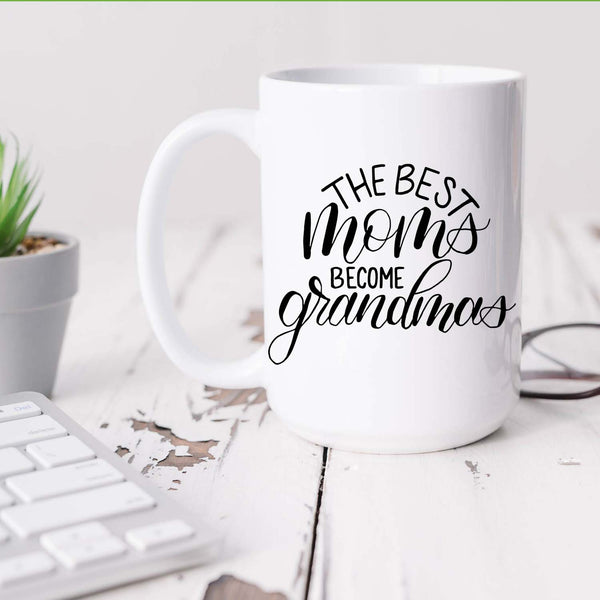 15oz white ceramic mug with hand lettered illustrated design that says the best moms become grandmas shown sitting on a white office desk