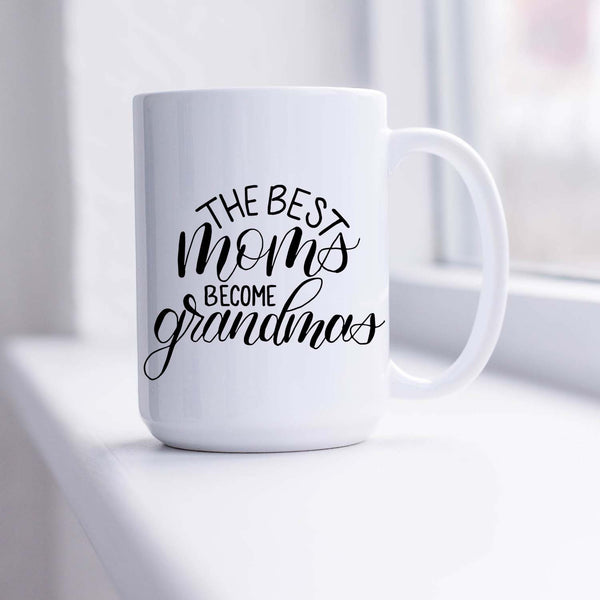 15oz white ceramic mug with hand lettered illustrated design that says the best moms become grandmas shown sitting in a sunny window