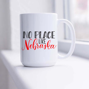 15oz white ceramic mug with hand lettered illustrated design that says No Place Like Nebraska shown sitting in a sunny window