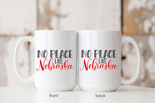 15oz white ceramic mug with hand lettered illustrated design that says No Place Like Nebraska showing front and back of the mug