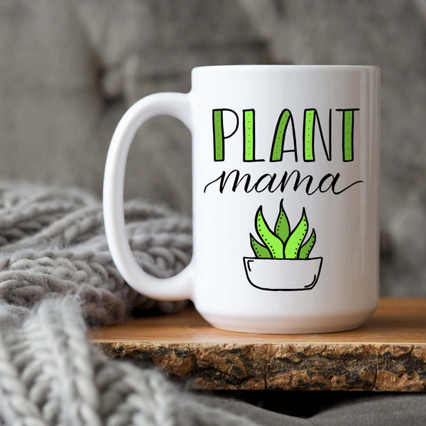 15oz white ceramic mug with hand lettered illustrated design that says Plant mama with the illustration of a succulent with green leaves shown sitting on a wood tray with a grey knit blanket