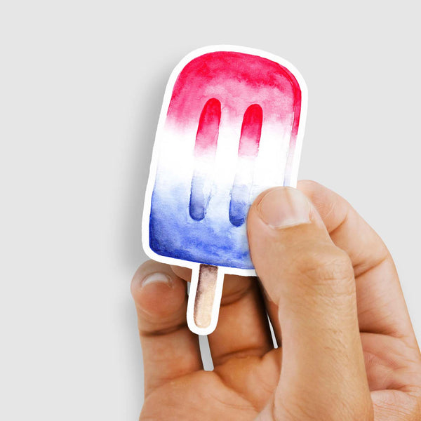 3" vinyl sticker of a watercolor painted red, white and blue patriotic popsicle shown with a woman's hand holding the sticker