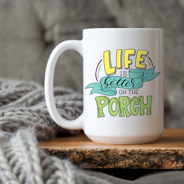 15oz white ceramic mug with hand lettered illustrated design that says Life Is Better On The Porch with a grey knit blanket