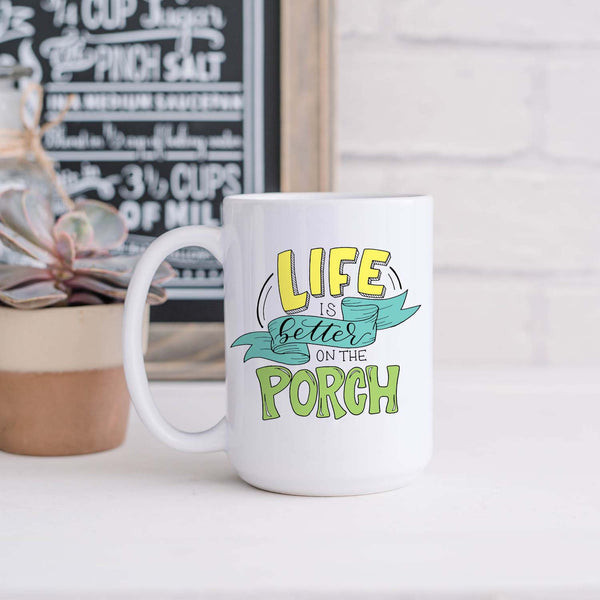 15oz white ceramic mug with hand lettered illustrated design that says Life Is Better On The Porch shown in a kitchen with plant